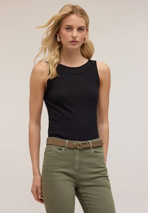 Top sin mangas negro acanalado combinado con pantalones verde oliva y un cinturón marrón claro. La modelo lleva pendientes redondos texturizados. Fondo neutro.