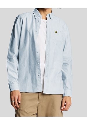 Person wearing a light blue and white striped button-up shirt over a white t-shirt with beige pants, no visible face or background details.