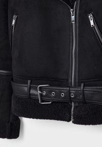 Veste en daim noir avec un ourlet doublé de shearling, dotée de fermetures éclair argentées, d'une ceinture amovible à la taille et de manches texturées.