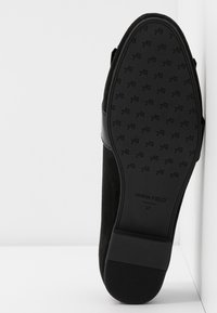 Semelle de chaussure en suede noir avec une base en caoutchouc texturée arborant un motif de petits logos. Nom de la marque "ANNA FIELD" et taille "37" imprimés dessus.