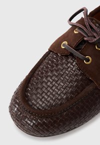 Brune skinnsko med et vevet mønster ved tåen, semskede detaljer, gullsnører og brune lisser. Rund form med en sydd kant.