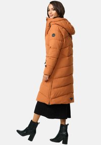 Long orange puffer coat with a hood, featuring a diagonal quilted design and side zipper. Paired with a black ribbed skirt and ankle boots.