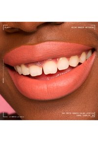 Close-up of smiling lips with coral matte lipstick on brown skin, showing natural teeth and smooth lip texture.