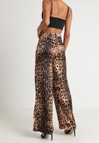 Läppäring-mönstrade vida byxor tillverkade av slät tyg, med hög midja och lös passform. Designen inkluderar svarta och bruna mönster.