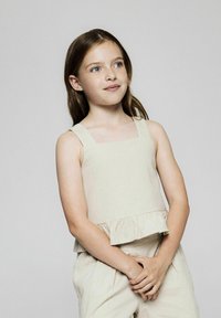 Beige ärmlös topp med fyrkantig halsringning och volangnedrekanter. Tillverkad av lätt tyg, i kombination med ljusa byxor.