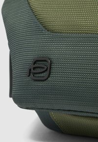 Grüne und oliv texturierte Stofftaschenecke mit einem schwarzen Markenlogo. Verfügt über glatte Kanten und ein strukturiertes Design.