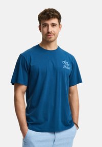 Camiseta de algodón azul con cuello redondo, mangas cortas y un diseño impreso en el lado izquierdo del pecho que dice "libera tu mente."