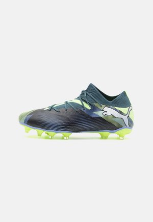 Crampon de football Puma bleu foncé et vert néon avec laçage à l'avant, tige texturée et semelle cloutée pour terrain ferme.