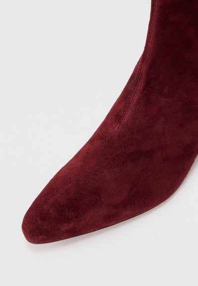 Bottines en suede bordeaux à bout pointu et texture lisse, présentant une silhouette élégante et des détails de couture minimalistes.