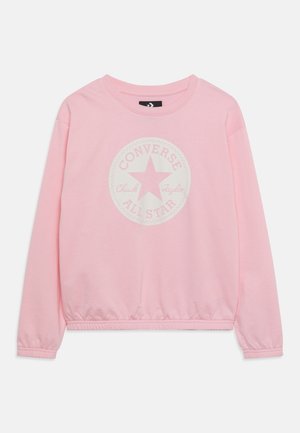 Sweat-shirt rose clair à manches longues avec poignets et ourlet élastiques, avec un logo circulaire Converse All Star blanc délavé sur la poitrine.