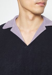 Pull en tricot marine avec un col en tissu éponge lavande contrastant, présentant un design en V et une texture douce.