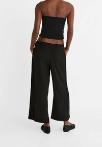 Zwarte strapless top gecombineerd met zwarte broek met wijde pijpen. De broek heeft een gestructureerde stof en een elastische tailleband voor comfort.