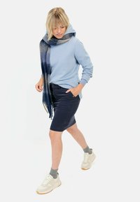 Helle blaue Kapuzenjacke, dunkelblautiger Jeansrock, geschichteter blau-grauer Schal, helle Turnschuhe mit Gummisohlen und graue Socken.