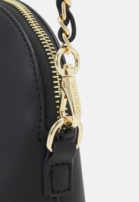 Černá kožená kabelka s bronzovým zipem a kovovými prvky, s propleteným řetízkovým popruhem a značkovým štítkem na zapínání.