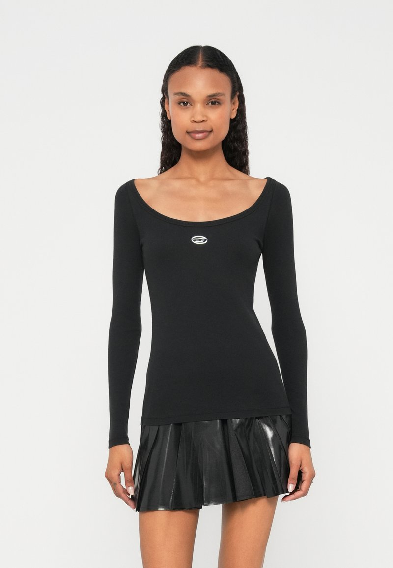 Μαύρο τοπ με μακριά μανίκια, στρογγυλή λαιμόκοψη και ασημί λογότυπο στο κέντρο. Συνδυάζεται με μαύρη πλισέ φούστα από δερματίνη.