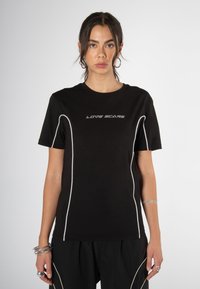 Schwarzes Baumwoll-T-Shirt mit kurzen Ärmeln, mit weißen Akzentnähten und dem Text "LOVE SCARS" in fetter Schrift über der Brust.