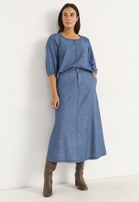 Jeansset bestående av en lös, kortärmad topp med rund halsringning och en lång kjol med hög midja och framlådor.