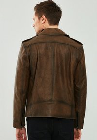Veste en cuir marron avec un col structuré et des détails cousus, dotée de zips sur les côtés et d'une surface lisse et texturée.