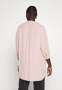 Długo rękawowa, jasnoróżowa bluzka z plisą na plecach, miękka w dotyku, z zapięciem na guziki przy mankietach i zaokrąglonym dołem. Posiada prosty, klasyczny design.