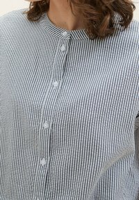 Knappet skjorte med rund krave, vertikale blå og hvide striber, letvægtsstof og synlige hvide knapper foran.