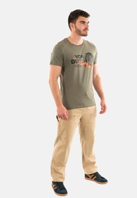 Una camiseta verde oliva con un estampado gráfico, combinada con pantalones cargo beige y zapatillas marinas con acentos naranjas. Un atuendo simple y casual.