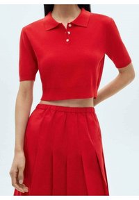 Polo rojo de punto con mangas cortas y cuello, que presenta un tapeta de tres botones, combinado con una falda roja con plisados. Textura suave en todo.