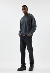 Hoodie nero tie-dye con una vestibilità ampia e orlo grezzo, abbinato a jeans scuri e sneaker nere testurizzate. Design semplice e casual.