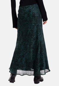 Falda maxi de patrón verde con una silueta fluida, hecha de tejido ligero. Presenta un dobladillo con una capa transparente y sutiles toques de brillo.