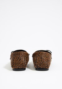 Zapatos tipo slip-on con estampado de leopardo, hechos de un tejido marrón texturizado, que presentan una suela negra baja y ligeros acentos elásticos para mayor comodidad.
