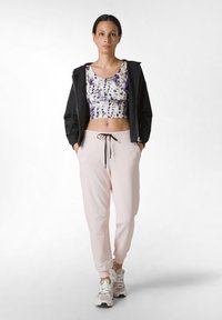 Svart zip-up jacka, flerfärgad kort topp med lila och grön mönster, ljusrosa joggers och vita sneakers med grå detaljer.