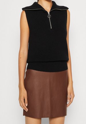 Un pull sans manches noir avec un large col et une fermeture éclair à l'avant, associé à une mini-jupe en cuir marron avec une texture lisse.