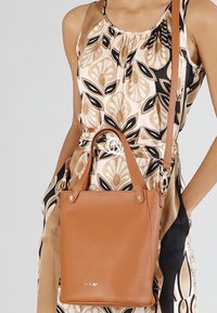 Brun läderhandväska med en strukturerad design, korta handtag och en avtagbar axelrem. Utrustad med detaljer i guldfärg och en diskret logotyp.