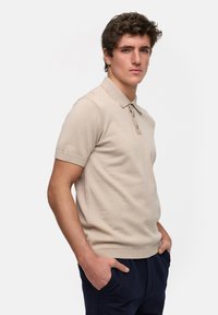 Beige kortermet polo skjorte med strikket tekstur, ribbede mansjetter og tre knapper foran, satt sammen med marineblå bukser.