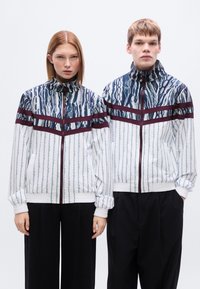 Ελαφριά μπουφάν με φερμουάρ από απαλό ύφασμα, με μπλε και λευκό αφηρημένο μοτίβο και μπορντό ρίγες στο στήθος.