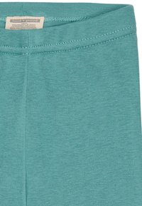 Turkooise katoenmengsel legging met een gladde textuur, elastische tailleband en vlakke stiksels. Het label is zichtbaar aan de bovenkant.