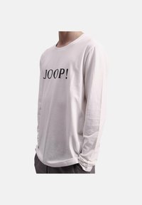 Valkoinen pitkähihainen T-paita, joka on valmistettu puuvillasta ja jossa on musta painettu logo "JOOP!" edessä. Yksinkertainen, rento leikkaus.