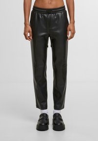 Černé kalhoty z umělé kůže s tapered střihem, elastickým pasem a stahovací šňůrou. Hladký povrch s detailem předního švu, v kombinaci s platformovými mokasíny.