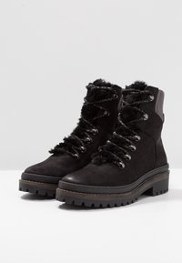 Botines de ante negro con ribete de piel sintética, ojales plateados y suela de goma gruesa con surcos para mayor tracción. Diseño de cordones.