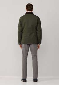 Chaqueta verde acolchada con cuello de pana marrón, botones a presión y corte holgado, combinada con pantalones grises y zapatos negros.