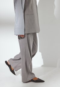 Abito grigio su misura con pantaloni a gamba larga e camicia a righe azzurro chiaro e bianca. Le scarpe flat nere a punta con un accento metallico completano il look.