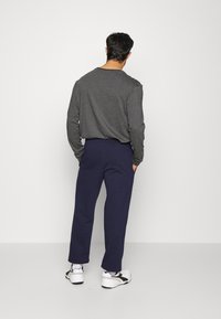 Maglietta grigia a maniche lunghe, pantaloni blu navy e sneakers bianche. La maglietta ha un collo a giro e i pantaloni sono leggermente stretti con tasche laterali.