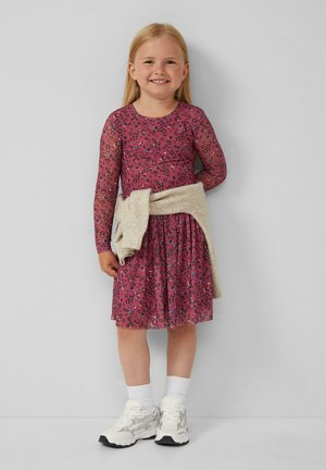 Abito a maniche lunghe di colore rosa con fantasia floreale e gonna svasata, abbinato a un maglione beige legato in vita e sneaker bianche con dettagli grigi.