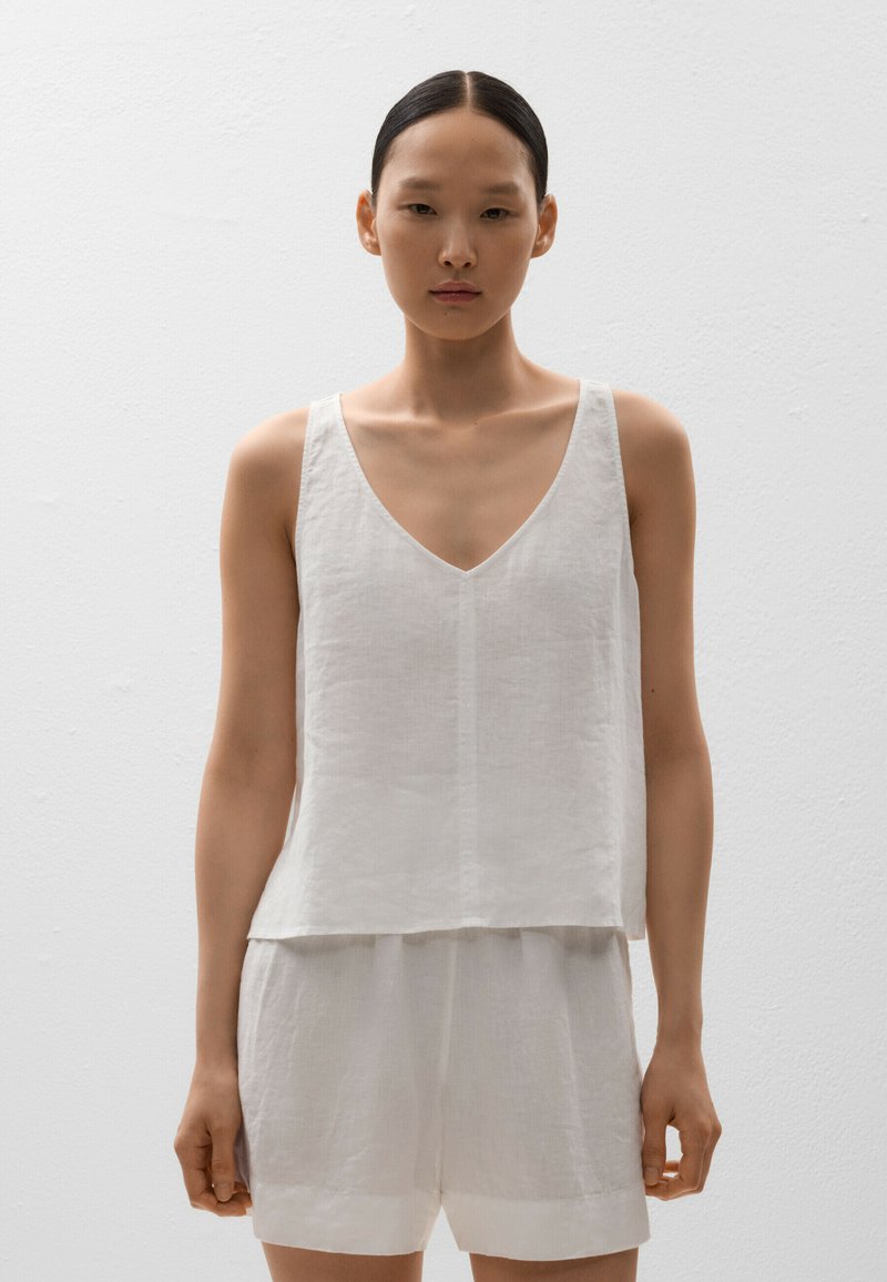 Top din in cu bretele alb din in, cu decolteu în formă de V și croială lejeră, combinat cu pantaloni scurți alb din in asortați. Textură netedă, design minimalist, fără modele.