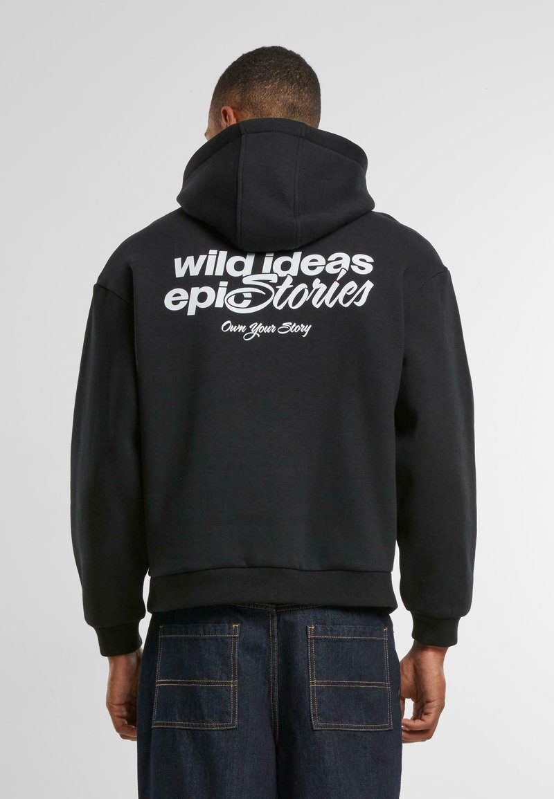 Schwarzer Kapuzenpullover mit Kängurutasche, auf der Rückseite mit großen weißen Buchstaben bedruckt. Der Stoff ist weich und hat gerippte Bündchen und Saum.