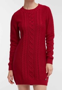 Robe tricotée rouge avec un col rond, comportant des motifs en relief sur le devant et des poignets et un ourlet côtelés. Longueur courte avec une texture lisse.