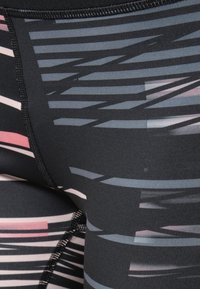 Gros plan sur un legging de sport noir avec des motifs abstraits de rayures horizontales rose, gris et violet et des coutures visibles le long des coutures.