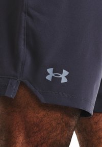 Tmavě modré sportovní šortky vyrobené z texturované tkaniny, s menším světle modrým logem Under Armour na dolní levé straně a bočními rozparky.