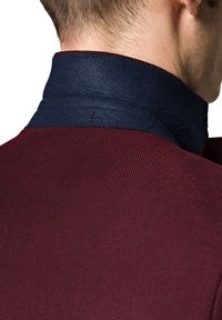 Męska kurtka z ciała o teksturowanej tkaninie w kolorze bordowym i kontrastowym, ciemnoniebieskim kołnierzu z filcu. Kołnierz ma widoczne detale szycia.