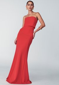 Punainen olkaimeton mekko, jossa on tiukka vartalo-osa ja levenevä helma. Valmistettu sileästä kankaasta, jossa on yksinkertainen muotoilu ja minimaalinen koristelu.