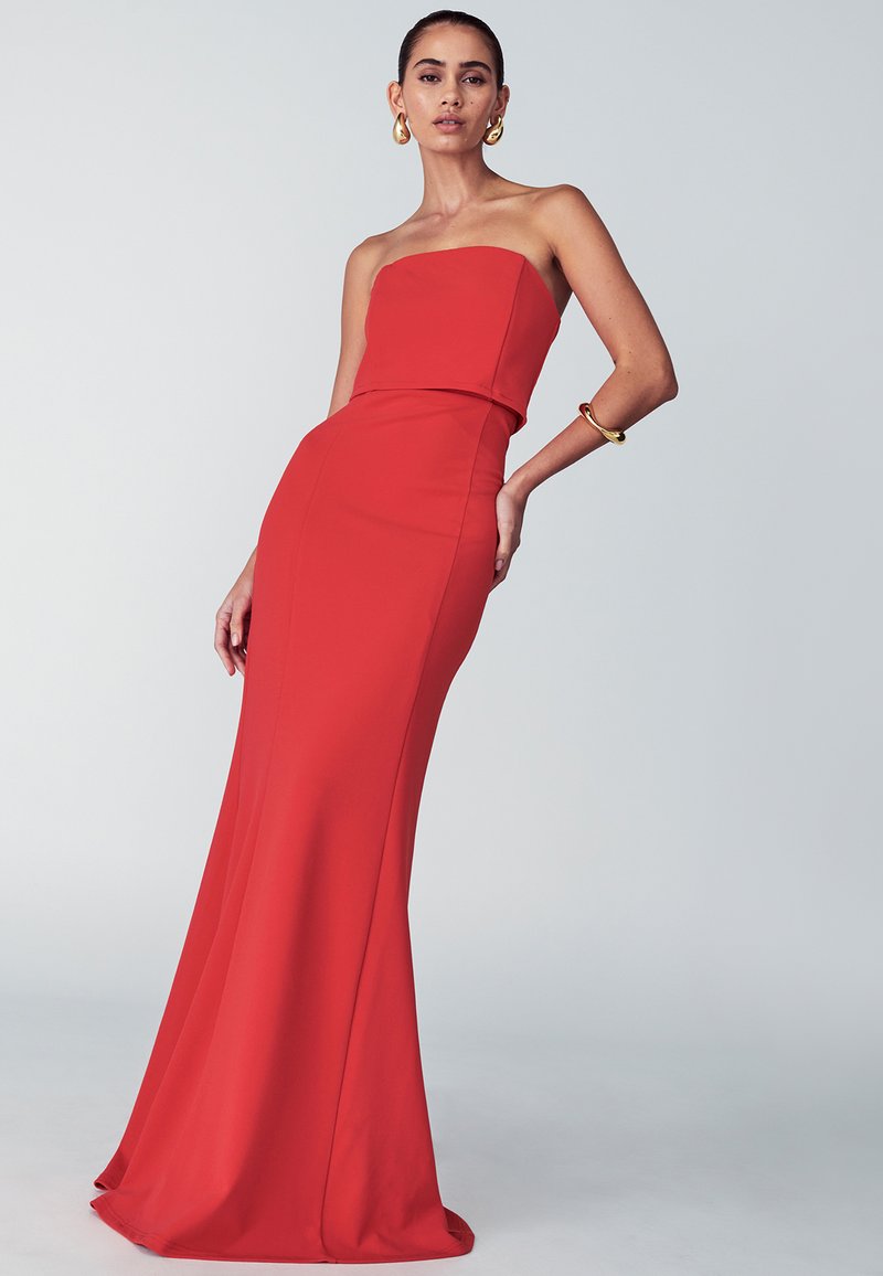 Punainen olkaimeton mekko, jossa on tiukka vartalo-osa ja levenevä helma. Valmistettu sileästä kankaasta, jossa on yksinkertainen muotoilu ja minimaalinen koristelu.